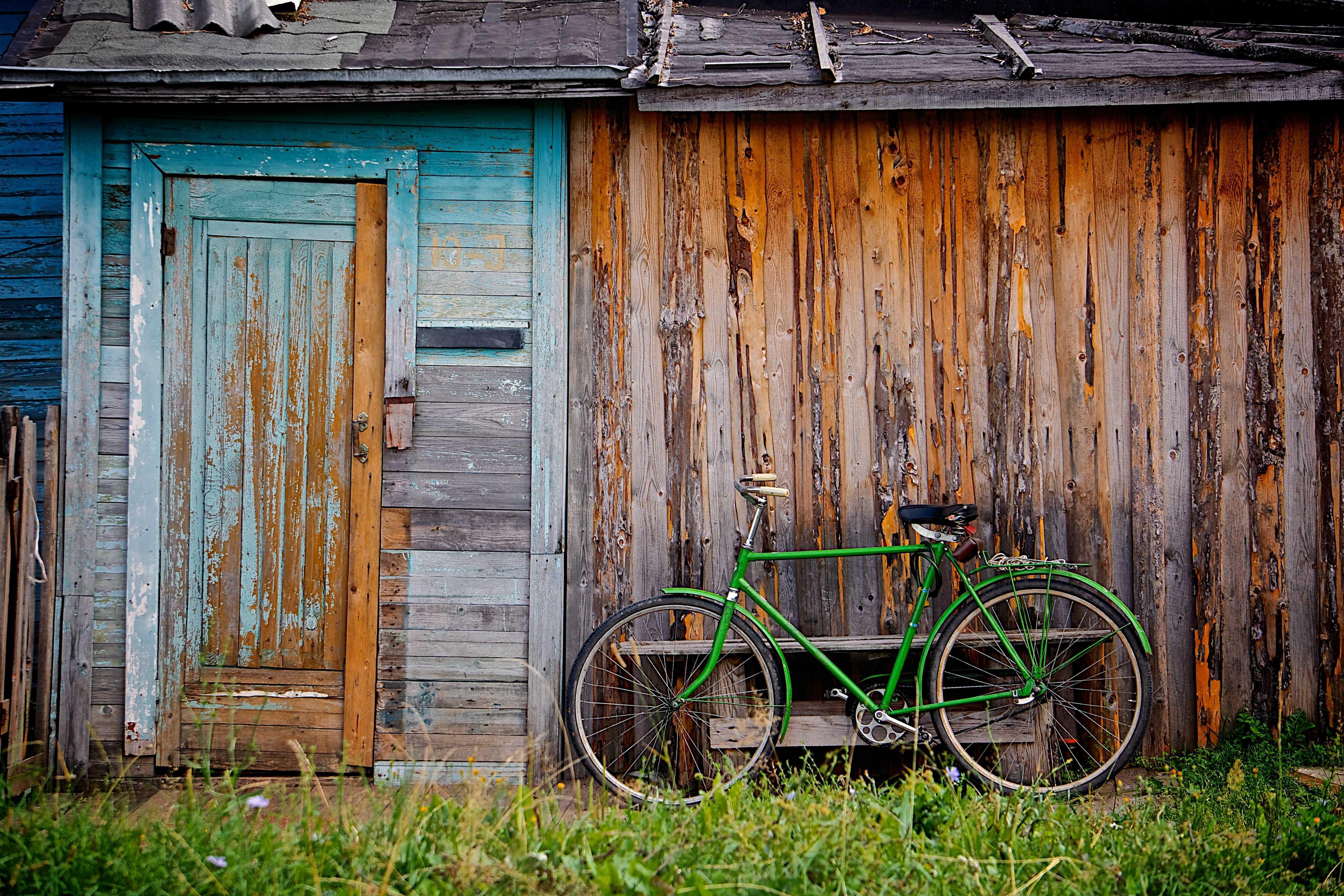 Ein grünes Fahrrad lehnt an einer alten Holzhütte.